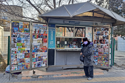 Beijing, China - February7, 2023: Man with mask standing by street newspaper stand amid coronavirus pandemic, Beijing, China.