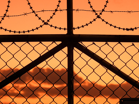 Razor wire, barbed wire and wire mesh fences surrounding Sydney Kingsford-Smith Airport. The corner of an exclusion warning sign attached to the fence is visible at the bottom right.  This image was taken from near Shep's Mound, a public viewing area off Ross Smith Avenue, at sunset on 5 February 2023.