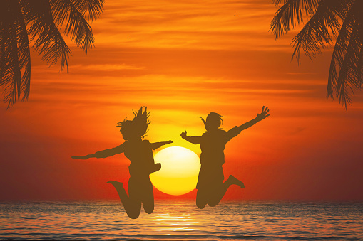 two women jumping at sea during sunset