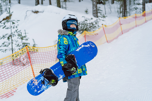 little boy learning to ride on snowboard climbing up ski slope. Winter leisure. Pine forest on background. High quality photo