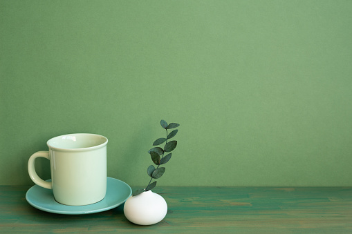 Coffee cup and eucalyptus leaf on wooden table. green wall background. minimal, copy space