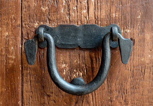 Close up of a black old door handle over a brown wooden door