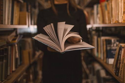 An unrecognizable librarian holds a book in her hands and turns the pages