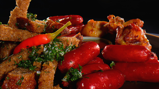 Fried meat fillets and sausages seasoned with herbs and red hot chili peppers - black background