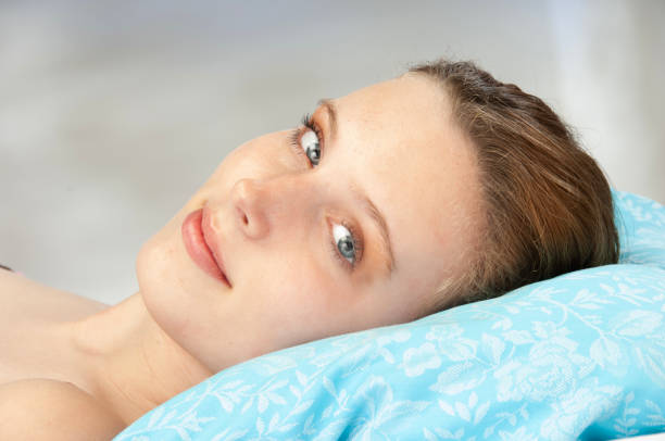 Smiling caucasian blond young woman hugging white duvet in the morning.