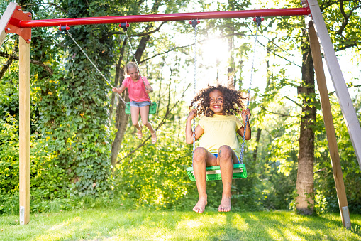 Girls swinging on swing in domestic garden during sunny day.