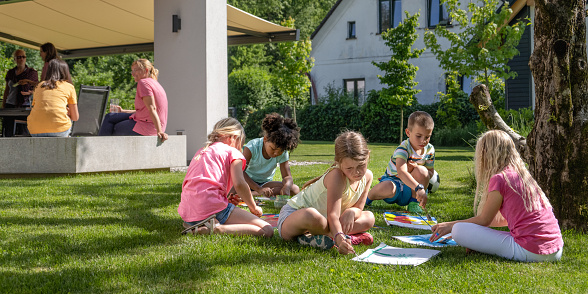 Children drawing picture on papers in garden during sunny day.