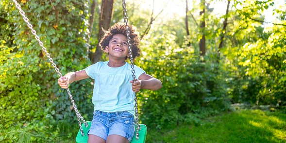 Smiling girl swinging on swing in domestic garden during sunny day.