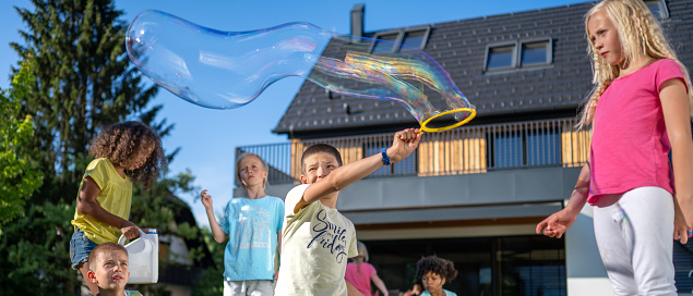 Group of kids playing with bubble wand in back garden during sunny day.