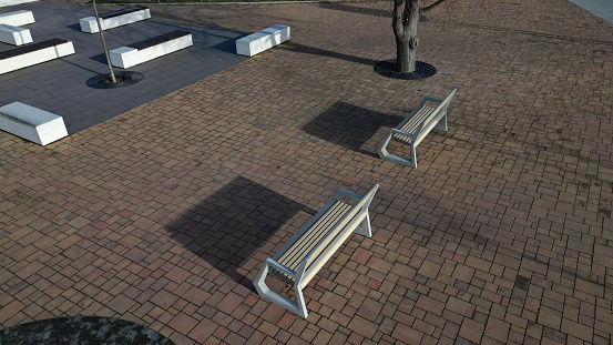 concrete white bench block and wave shape in the park on a dark cobbled square, clean concrete surface gray brown white pedestrian and rest area at skate park for young people, above teenagers, bench, terrace, building, street