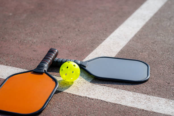 pickleball-spiel, buntes orangefarbenes und graues pickleball-paddel mit gelbem ball, outdoor-sport-freizeitaktivität. - racketball racket ball court stock-fotos und bilder
