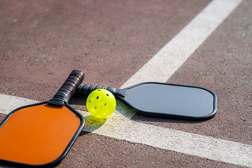 pickleball game, colorful orange and grey pickleball paddle with yellow ball , outdoor sport leisure activity