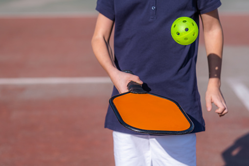 Pickleball paddle and yellow ball close up in children hands, leisure outdoor sport activity