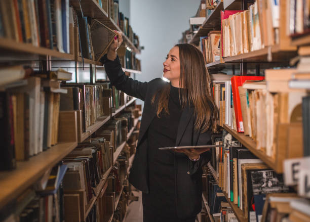 istock The librarian takes a book from the shelf while holding digital tablet in her hands 1463666543