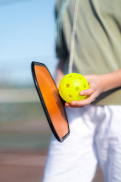 Pickleball paddle and yellow ball close up in children hands, leisure outdoor sport activity. stock photo