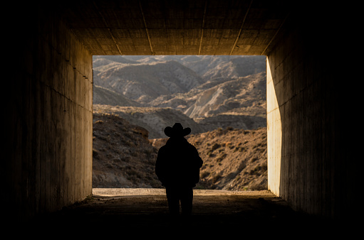Silhouette of adult man in cowboy hat in tunnel in desert. Almeria, Spain