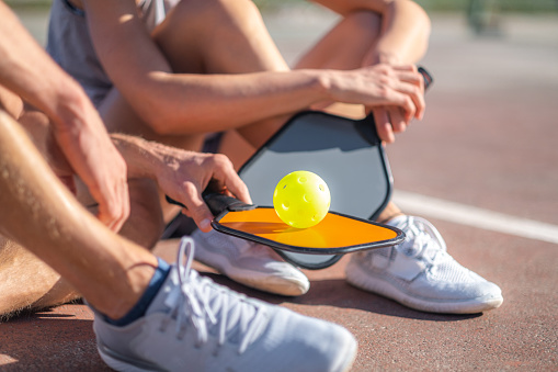 pickleball game, relaxing pickleball players couple with yellow ball with paddle sitting after game, outdoor sport leisure activity