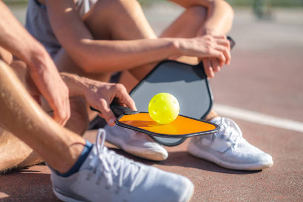 pickleball game, relaxing pickleball players couple with yellow ball with paddle sitting after game, outdoor sport leisure activity. stock photo