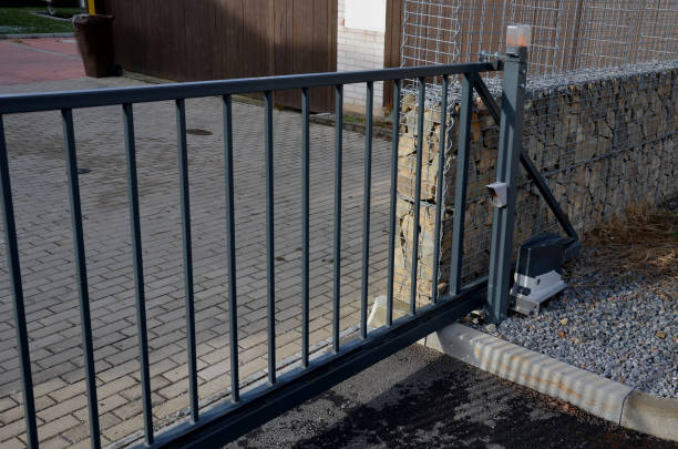 ingresso al cortile al parcheggio attraverso un cancello scorrevole basso. il cancello si muove lateralmente lungo la rotaia. c'è un faro lampeggiante arancione sul palo. il telecomando gira cancello scorrevole, nero - garden fence flash foto e immagini stock