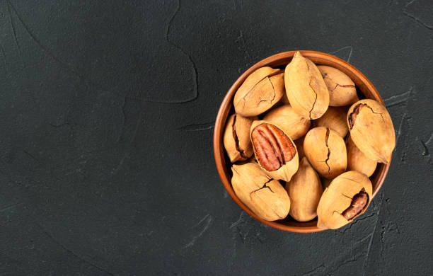 istock Ceramic bowl hollow of dry shelled pecans on a dark concrete background, copy space 1463669842