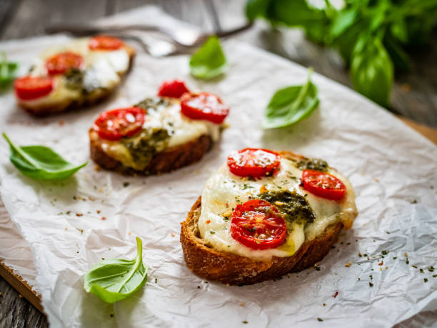 colazione bruschetta - mozzarella, pane, pesto e pomodori su tavola di legno - bun sandwich vegetable cream cheese foto e immagini stock