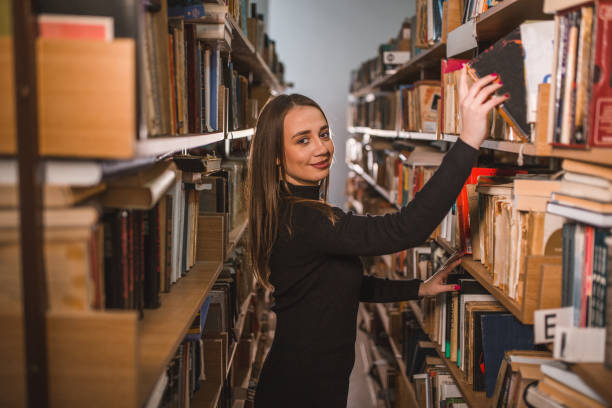 istock Gorgeous librarian takes a book from the shelf in the library and looking at camera 1463677102