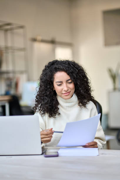 istock Young latin business woman holding documents working on laptop, vertical. 1463680772