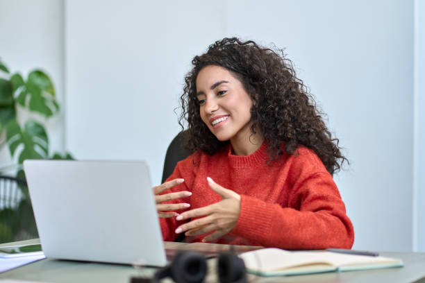 Happy latin business woman having video call hybrid meeting in office. Happy young latin business woman employee, hr manager having remote videocall work hybrid meeting or job interview talking to team or partner looking at laptop on virtual video digital call in office. remote location stock pictures, royalty-free photos & images