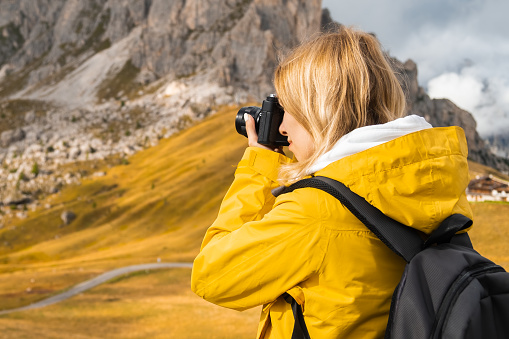 Woman takes photos of scenic Passo Giau pass. Traveler with backpack uses camera to capture Italian Alps