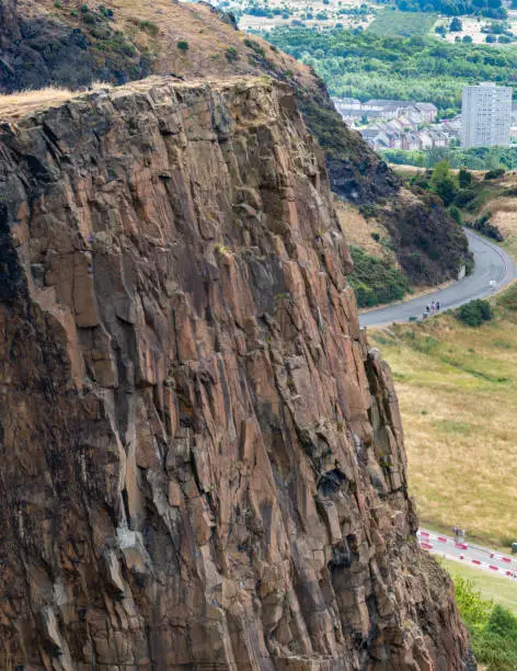 Looking down to pathways of Holyrood Park far below.narrow paths across sheer vertical cliff faces,dramatic views across the Scottish capital city,on a summer day.
