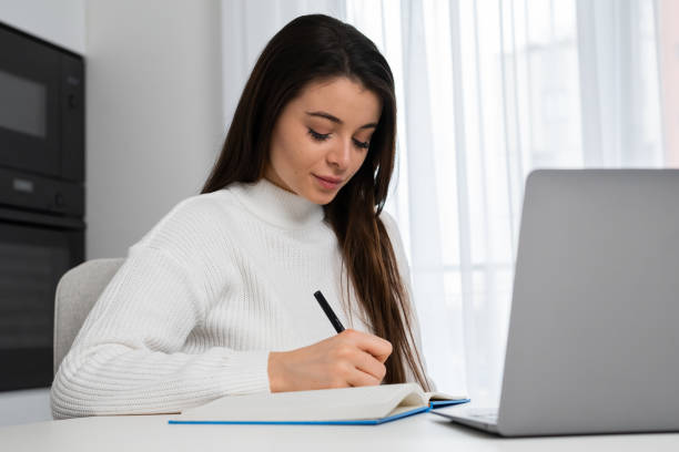 istock Intelligent female student writing notes to textbook sitting at home and preparing to exam 1463684009