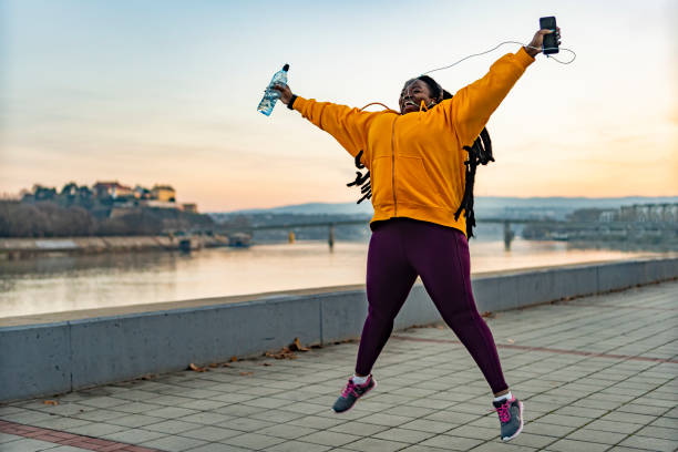 Sport women jumping and celebrating with arms raised. An African American woman jumping and celebrating with arms raised. weight loss stock pictures, royalty-free photos & images