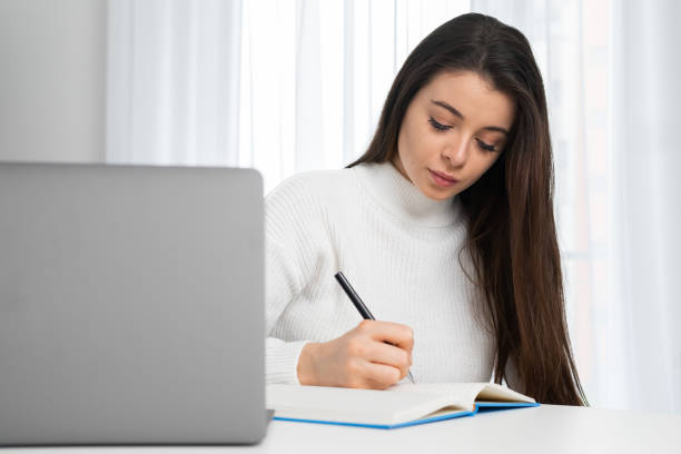 istock Young woman takes online courses via notebook making notes 1463684175