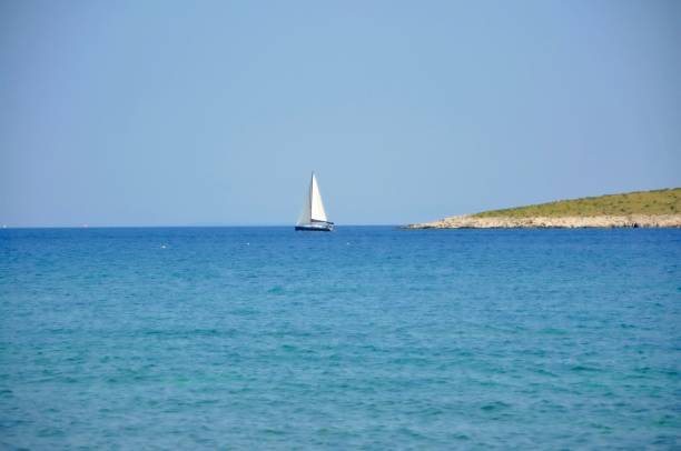 Sailing boat defront isolated island with open sails.Classic sailboat in a downwind leg. Floating yacht.Sailing ship luxury yacht with white sails in the Sea.