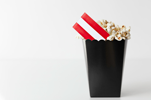 Black popcorn bag in front of white background with flag of Austria. Representing film industry in Austria.