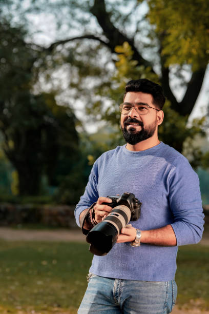 istock Young indian man holding camera in hand and giving expression at park 1463695044