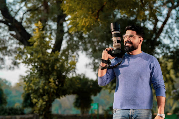 istock Young indian man holding camera in hand and giving expression at park 1463695671