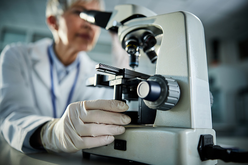 Close up of a female chemist working on a medical research through a microscope in laboratory.