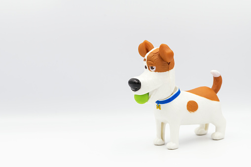 A statuette of a dog playing with ball isolated on a white background. Dog in profile from the side. Figure and children's toy in the form of a dog.