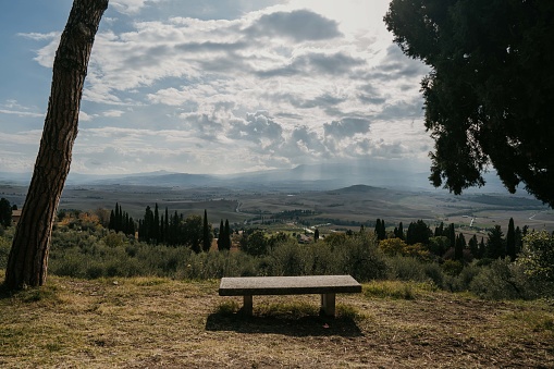 Bench overlooking scenic Tuscany landscape with hills and valleys on a cloudy day.