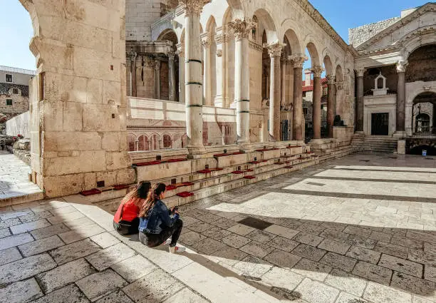 Two friends sitting on steps of Peristyle or Peristil of ancient roman palace built by emperor Diocletian in Split, Croatia.