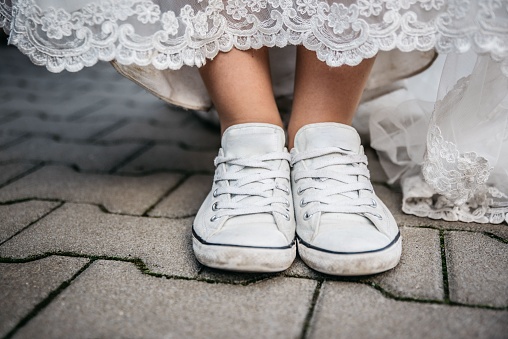 A closeup shot of the legs of a girl wearing white sneakers and lace dress standing on stone floor