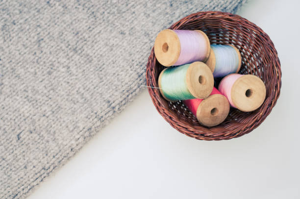 istock Basket of colorful sewing threads beside a grey fabric on a white table with free space for text 1463704611