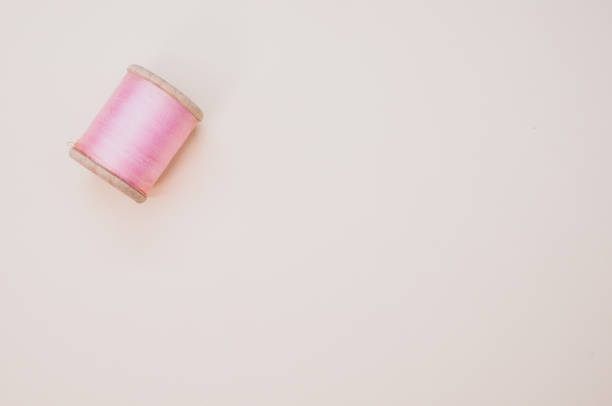A pink sewing thread isolated on a light background with free space for text