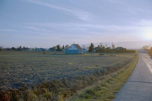 A rural asphalt road along a dry field with a detached house under a cloudless sky