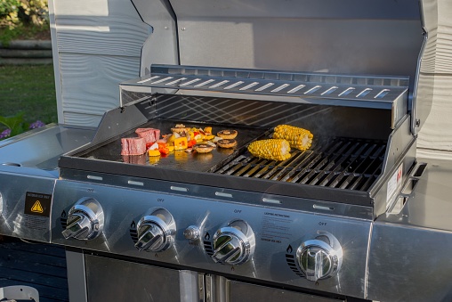 A gas barbeque grill stove in silver, cooking corn and delicious food in the outdoors