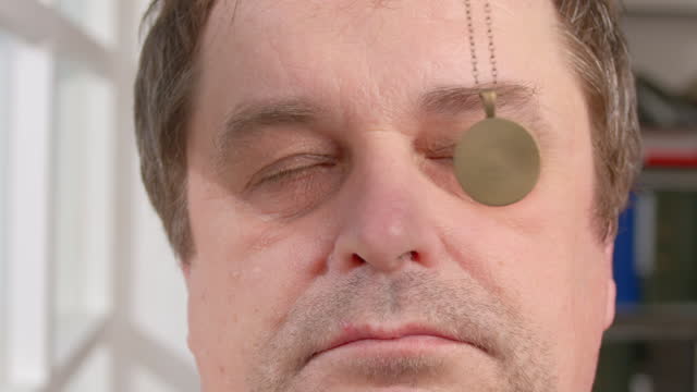 Portrait of man falls asleep in hypnosis session. Human eyes follow swinging hypnotic pendant on chain and close