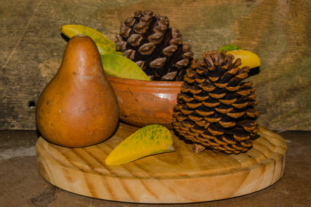 A wooden round board with pine cones, a pear, and leaves on it