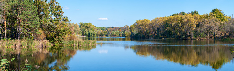 Autumn landscape on a sunny day, panorama of a park with yellow trees over a lake.