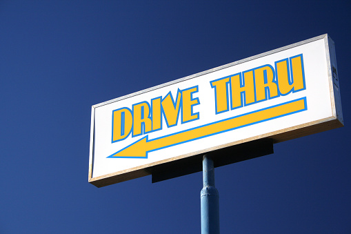 A low angle shot of a drive-thru sign at a restaurant with an arrow pointer under a clear blue sky
